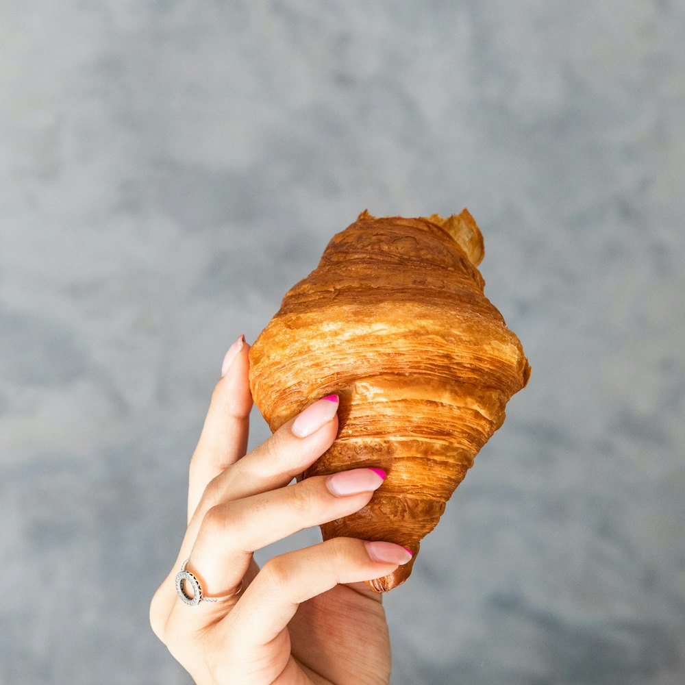 Hand holding a golden butter croissant against a grey wall