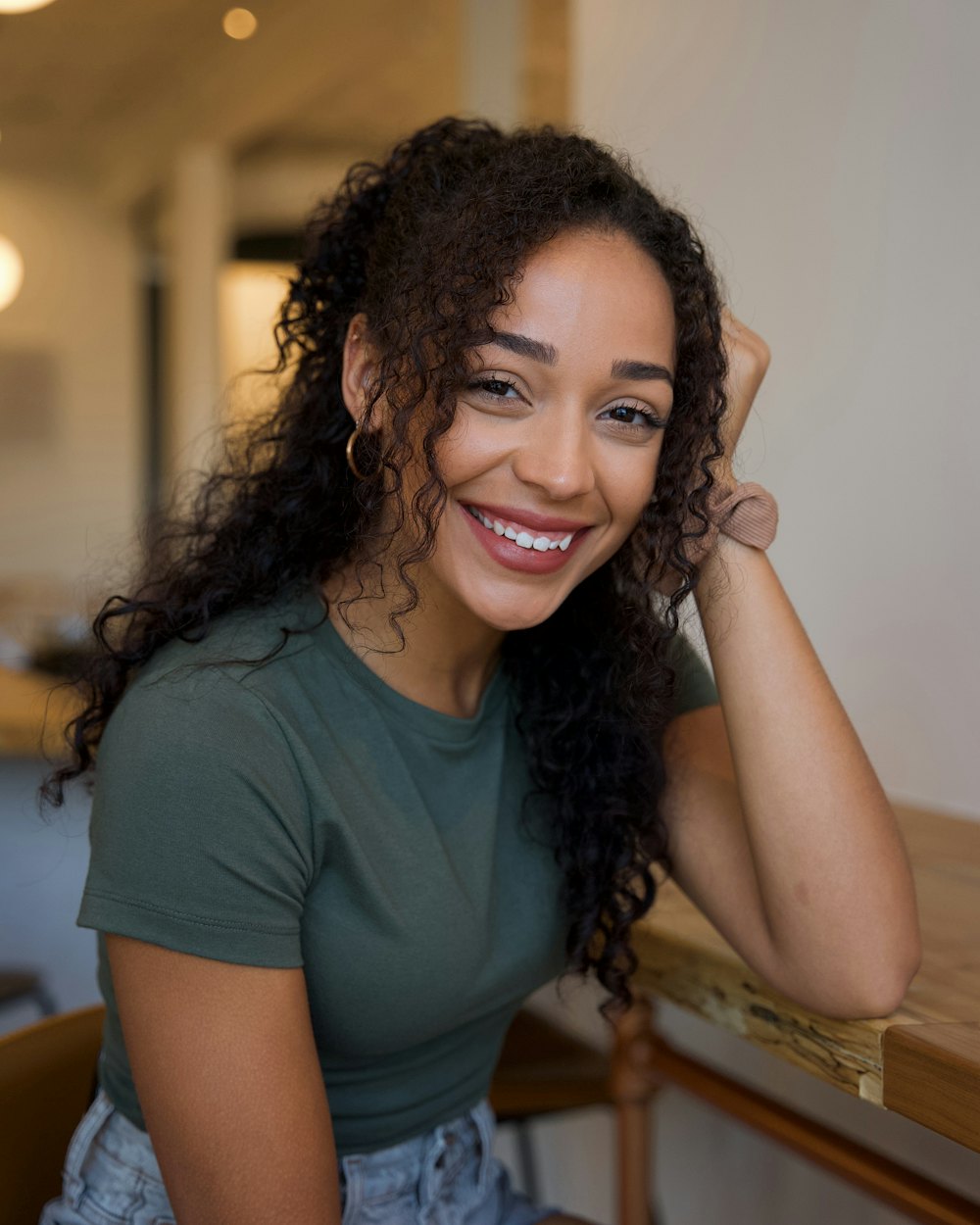 Smiling woman with curly hair sitting at a wooden table